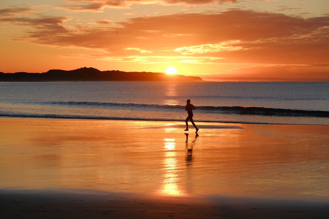 our-story A person running on a beach at sunrise in Australia, reflecting tranquil fitness and nature.