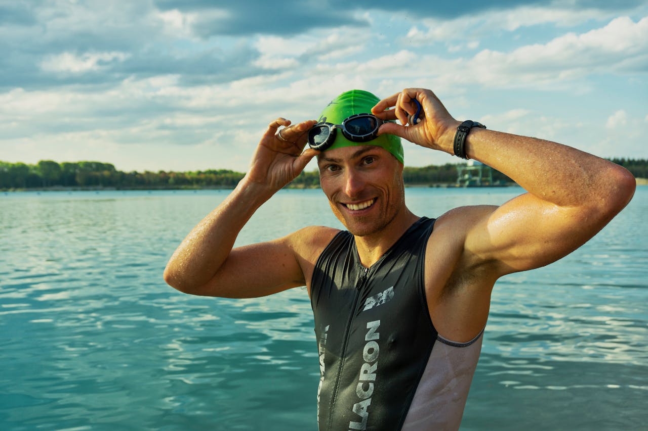 services-01 Confident male athlete adjusting goggles at a lake during a sunny day, ready for training.